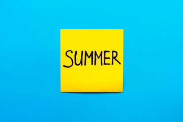 Close up black handwritten inscription summer on one yellow square sticker on blue background with copy spase
