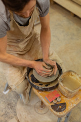 Hard-working skilled guy sitting on a wooden bench with pottery wheel