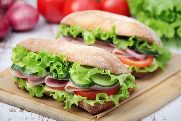 Two sandwiches with fresh vegetables, ham and cheese in ciabatta bread