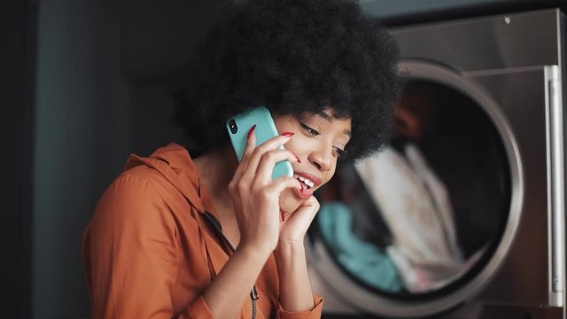 Smiling Young Woman Talking On Mobile Phone At Laundromat.