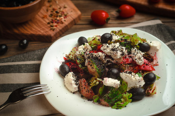 Mediterranean salad with homemade cheese, olives, edible earth, and sweet peppers. Cafe menu on a wooden background in warm colors with copy space.