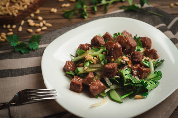 Braised beef with parsley, cucumbers, pine nuts and sweet onions. Cafe menu on a wooden background in warm colors with copy space.