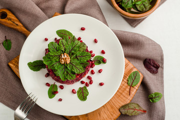 Beet salad with pomegranate, walnuts, prunes and spinach. Cafe menu on a wooden background in warm colors with copy space.