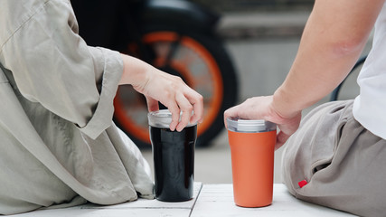Fototapeta premium Woman and man sit on white table with two lovely coffee cups in summer holiday, part of body, rear view, relationship concept.