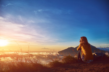 Woman enjoying nice landscape and sunrise from a top of mountain Batur, Bali, Indonesia.