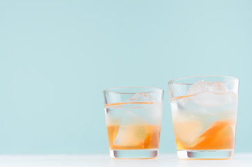 Tropical fresh layered cocktail with ice cubes, oranges liquor in misted shot glass  on pastel blue background.