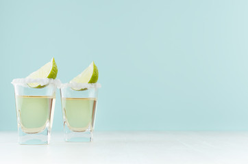 Golden mexican tequila shot drinks with salty rim, piece lime in elegant glass on pastel green...