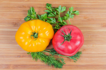 Pink and yellow tomatoes, greens on a wooden surface