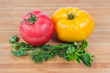 Pink and yellow tomatoes, greens on a wooden surface