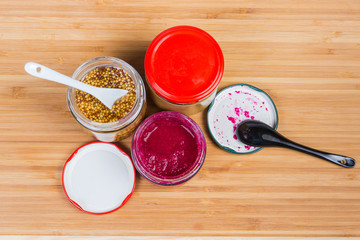 Various condiments in small glass jars on a wooden surface