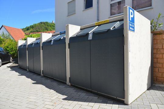 Eingebaute Abfallsammelbehälter-System mit Hinweisschild und Reflektoren an der gepflasterten Parkplatz-Zufahrt eines modernen städtischen Mehrfamilien-Wohngebäudes