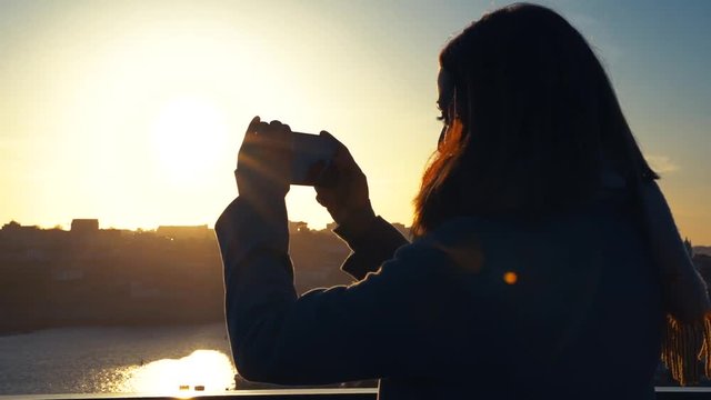 woman taking pictures with a high top technology phone. Perfect shot at sunset with bright colors and results. young female tourist taking pictures with her phone to the historic city of Oporto 