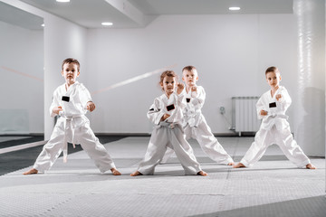Small group of Caucasian kids in doboks practicing taekwondo and warming up for treining while standing barefoot. - obrazy, fototapety, plakaty