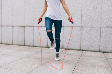 Young fitness woman rope skipping against city wall