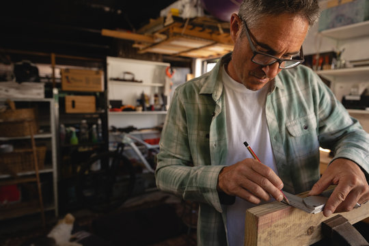 Carpenter using graduated square on wooden plank in workshop
