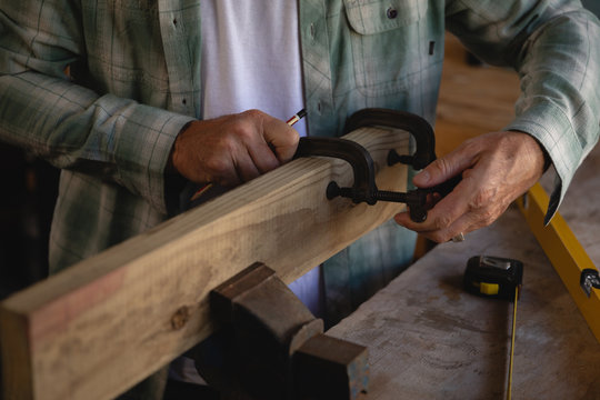Mature carpenter using clamp on wooden plank in workshop