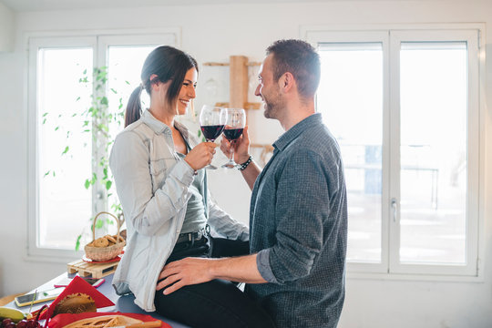 Engaged couple at a time of intimacy at home - Boyfriend and girlfriend toast with a glass of red wine - Wife and husband in their new home