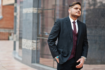 Stylish indian businessman in formal wear standing against windows in business center.