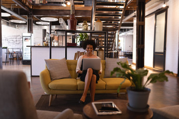 Happy businesswoman sitting on yellow sofa while she is using laptop