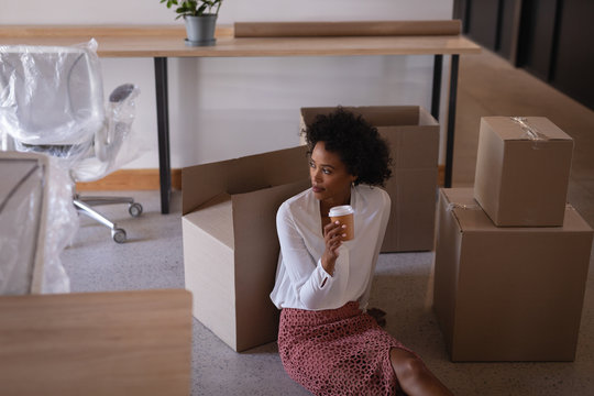Businesswoman having coffee while sitting on floor against cartons in office