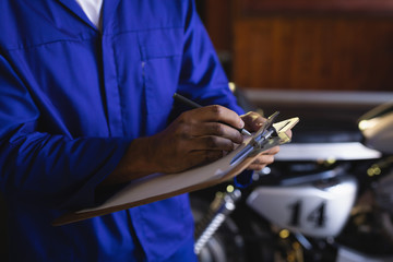 Bike mechanic maintaining automobile records on clipboard at garage 