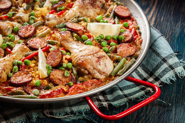 Traditional paella with chicken legs, sausage chorizo and vegetables served in paellera