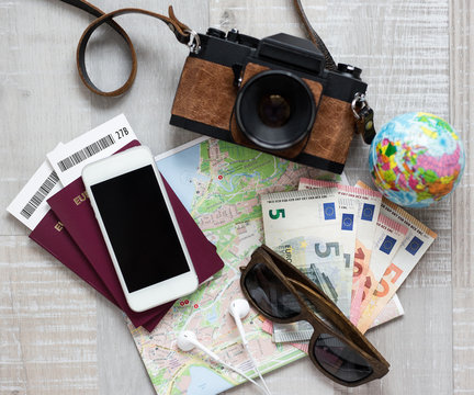 travel concept - top view of travel objects over wooden background - camera, map, money, passport, sunglasses and smart phone