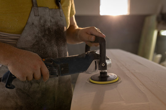 Man grinding surfboard in a workshop