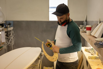Man measuring surfboard in a workshop