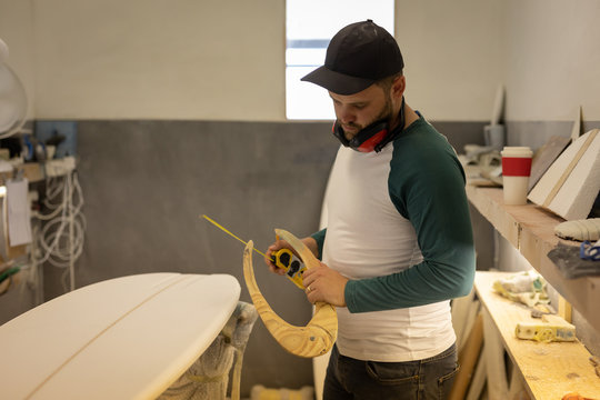 Man measuring surfboard in a workshop - Powered by Adobe