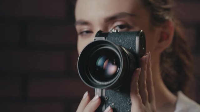 Pretty woman taking picture with vintage photo camera on brick wall background