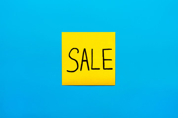 Trade, marketing, reminder and combination concept- Close up black handwritten inscription sale word on one yellow square sticker on blue background with copy spase, horizontal orientation