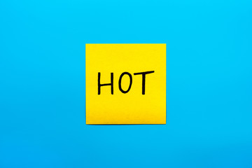 Seasons, summer, reminder and combination concept- Close up black handwritten inscription hot word on one yellow square sticker on blue background with copy spase, horizontal orientation