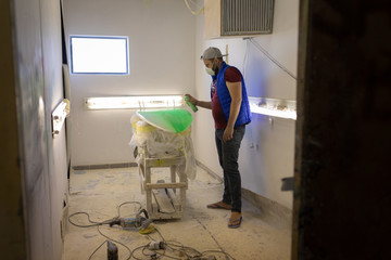 Man using spray paint on surfboard in workshop