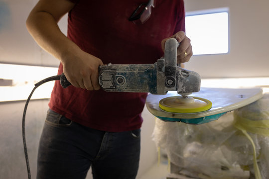 Man grinding surfboard in a workshop