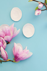Beauty background for cosmetic products and magnolia blossom on pastel blue background. Spring skin care plan, top view, flat lay. Cosmetics and skin care concept.