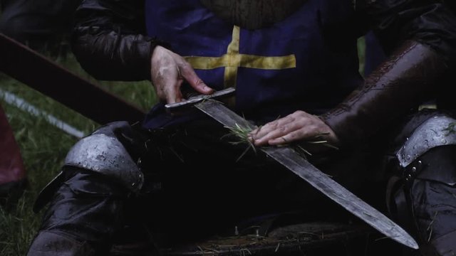Close up of a medieval soldier cleaning his sword with grass