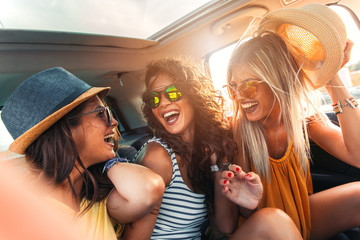 Three female friends enjoying traveling in the car. Sitting in rear seat and having fun on a road...