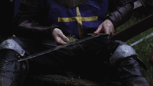 Medieval soldier is cleaning his sword under rain with grass, close up
