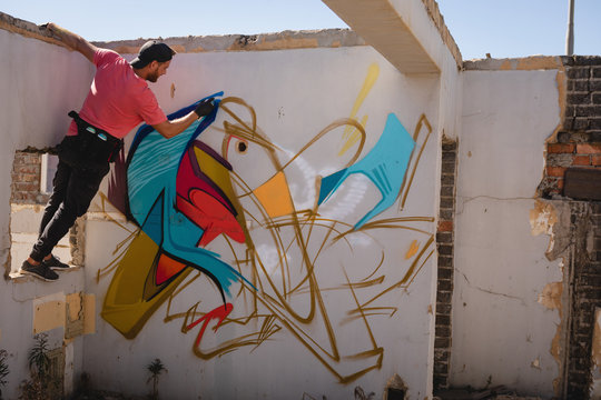 Graffiti artist spray painting on weathered wall 