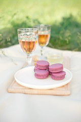 Light pink and fuchsia pink french macaroons or macaroons with glass goblets of pink wine in a round white plate on a beige tablecloth background with copy space.