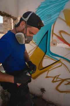 Graffiti artist standing with spray painting at alley room