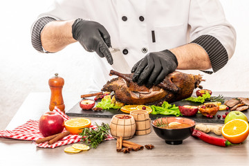 Roast Christmas duck with thyme and apples on rustic wooden table. Thanksgiving or Christmas Dinner. The chef is cutting the duck