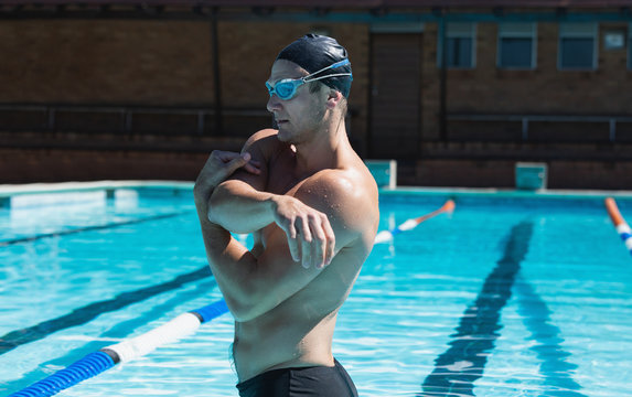 Young male swimmer with swim goggle stretching at swimming pool 