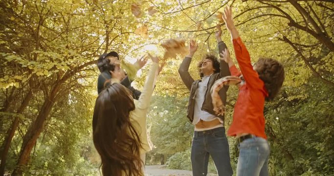 Happy young family of four standing in circle, looking at each other, and throwing golden leaves in the air 4k