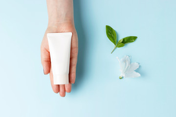 Tube with cream in female hand, blue background, top view, natural cosmetics concept