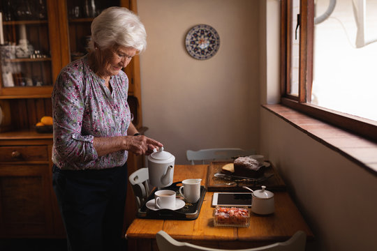 Active senior woman pouring coffee in a cup at dining table in kitchen at home