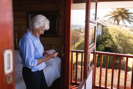 Happy active senior woman using mobile phone in bedroom at home