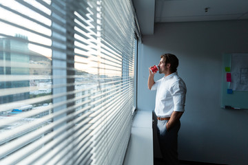 Young male executive with hand in pocket drinking coffee near window in a modern office