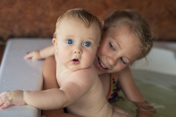 Two happy little children playing in the bath at the day time.